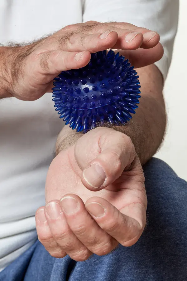 Ergotherapie-SonjaWandel-Stuttgart-Orthopaedie-Kugelball Orthopädie Ergotherapie: Erwachsener Arm mit hochgekrempeltem Hemdärmel hält einen blauen Noppenball in der Handfläche. Hintergrund neutral und verschwommen.