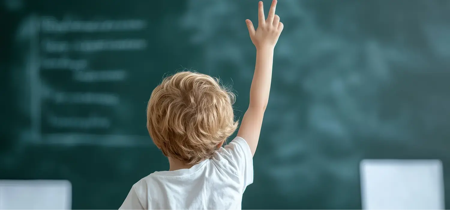 Ergotherapie-SonjaWandel-Stuttgart-Pädiatrie-Konzentration Pädiatrie Ergotherapie: Kind mit kurzen, hellbraunen Haaren sitzt auf einem Stuhl, Rücken zur Kamera. Der rechte Arm ist erhoben, die Hand zeigt nach oben. Hintergrund unscharf und hell.