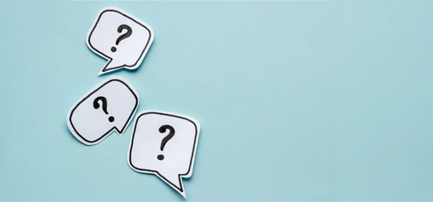 Drei ausgeschnittene Sprechblasen aus weißem Papier mit schwarzen Umrissen. Jede enthält ein großes schwarzes Fragezeichen. Die Sprechblasen liegen schräg angeordnet auf einer hellblauen Fläche.