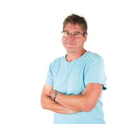 Marco Müller: Mann mit kurzen Haaren und Brille, trägt hellblaues T-Shirt, sitzt entspannt mit verschränkten Armen.