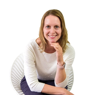 Nadine Uhlig: Frau mit schulterlangen Haaren, trägt weißes Oberteil, sitzt auf einem weißen Stuhl und stützt den Kopf mit der Hand.